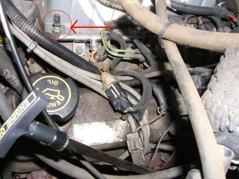 1990 Ford Bronco - A close-up view of various engine components, including hoses, wiring, and a sensor highlighted by a red arrow.