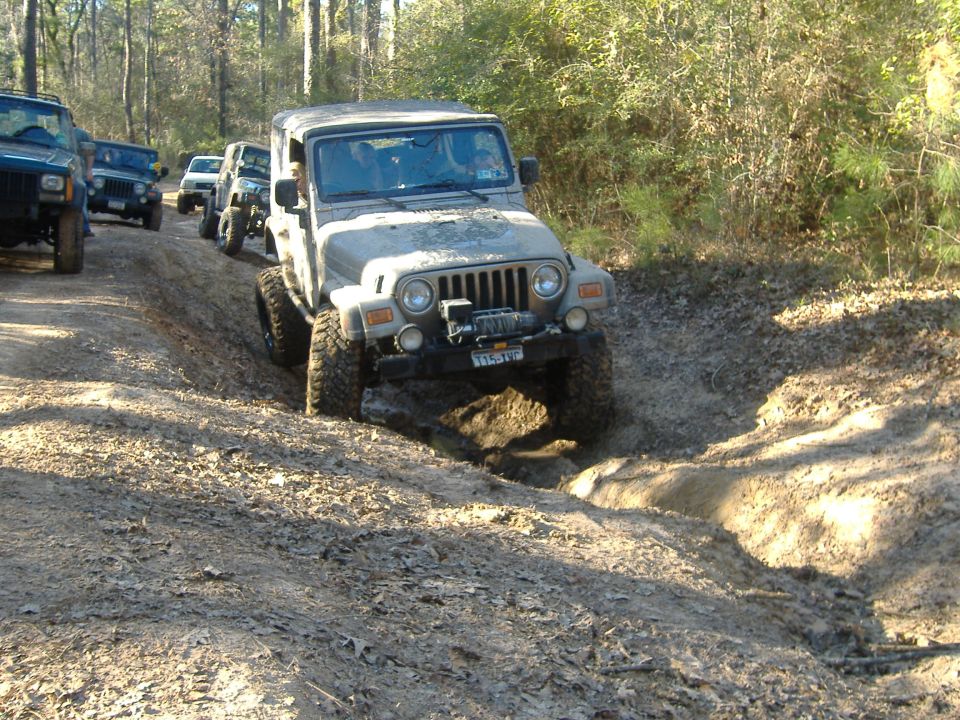 Tan 1999 Jeep Wrangler navigating a muddy off-road trail with other Jeeps behind
