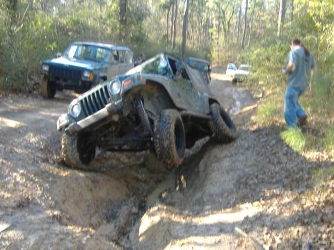 1999 Jeep Wrangler - Multiple vehicles navigate a challenging muddy off-road trail through a wooded area.
