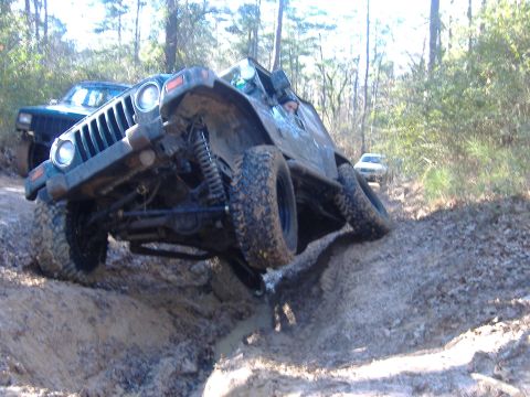 1999 Jeep Wrangler - A Jeep Wrangler navigates a challenging muddy off-road course with another vehicle behind it.