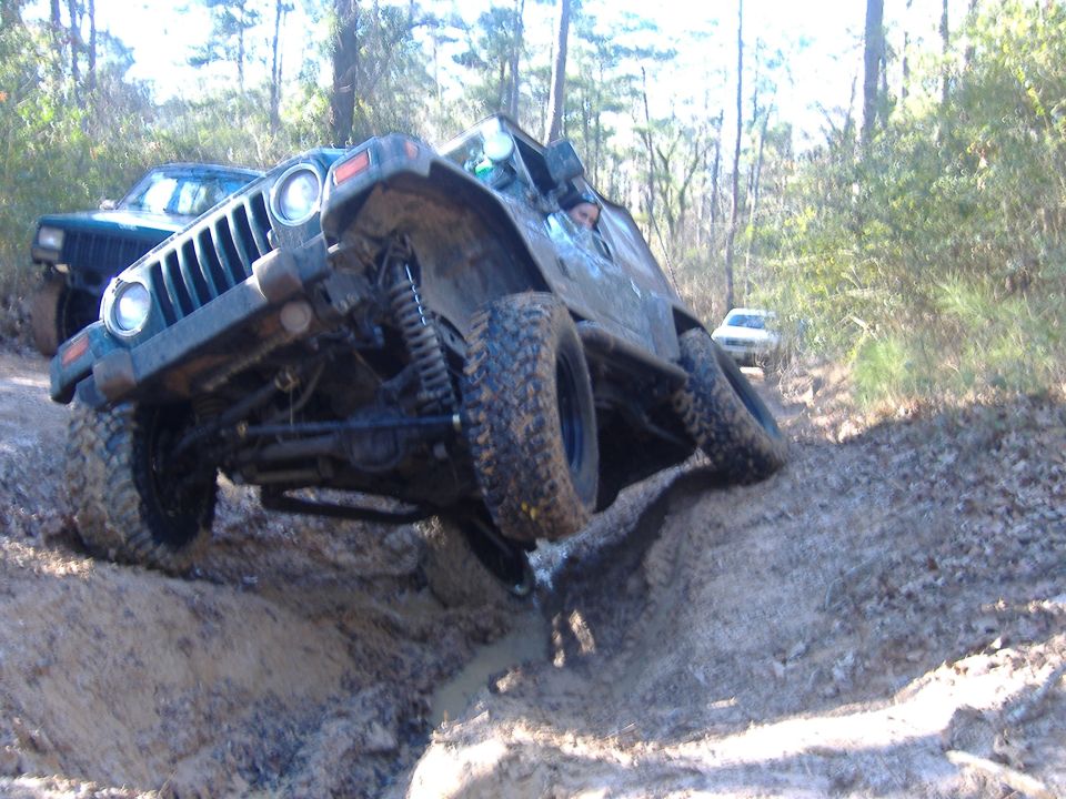 Dark green Jeep Wrangler tilted on a muddy trail, front grille visible