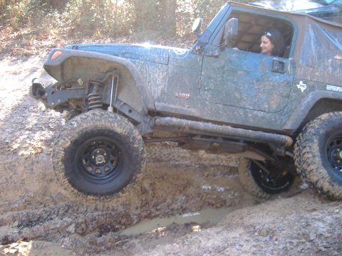 1999 Jeep Wrangler - A green Jeep Wrangler navigates a challenging muddy trail, its off-road capabilities.