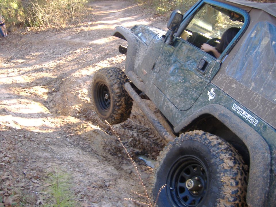 1999 Jeep Wrangler driving through a muddy trail, tires covered in dirt