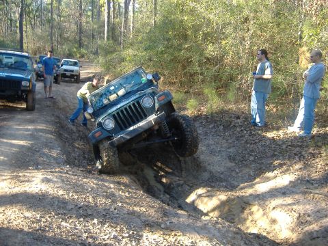 1999 Jeep Wrangler - A group of off-road vehicles navigate a muddy trail, with one Jeep struggling to maintain traction.