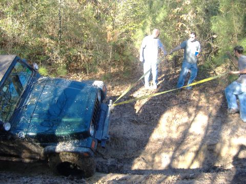 1999 Jeep Wrangler - A Jeep Wrangler is stuck in a muddy ditch while people attempt to pull it out with a strap.