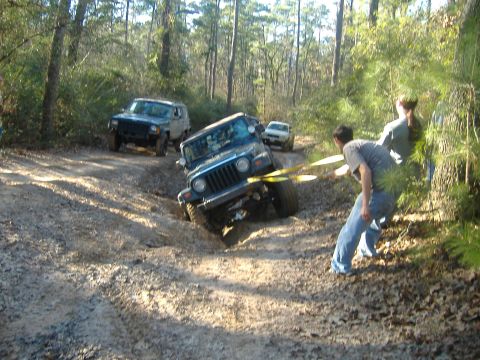 1999 Jeep Wrangler - A 1999 Jeep Wrangler is being towed out of a muddy ditch by another vehicle, with people assisting.