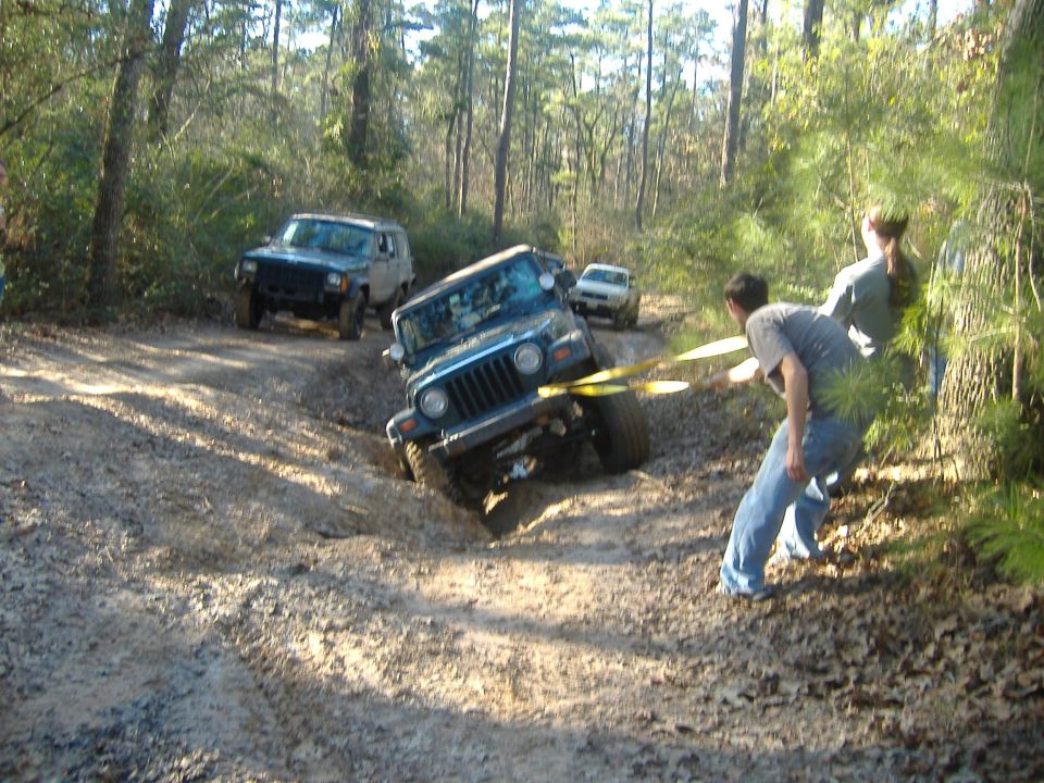 Blue 1999 Jeep Wrangler stuck in mud, being pulled by yellow straps
