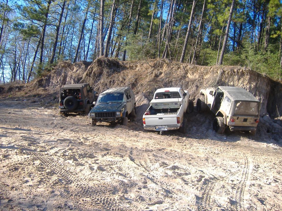 Four off-road vehicles on sandy terrain, including a Jeep Wrangler and two trucks