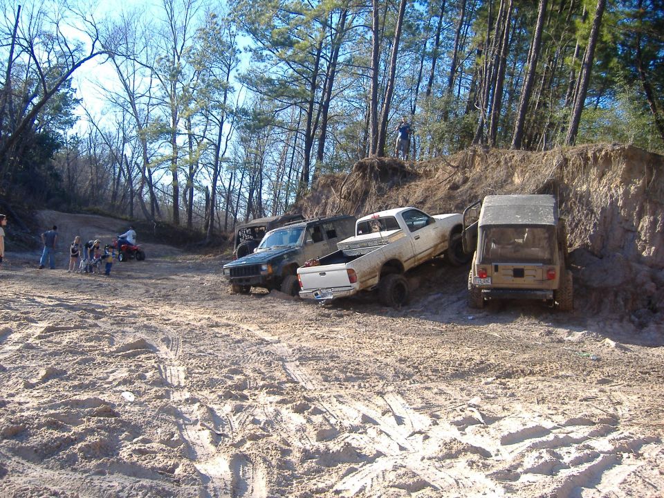 Multiple off-road vehicles navigating sandy terrain with trees in background