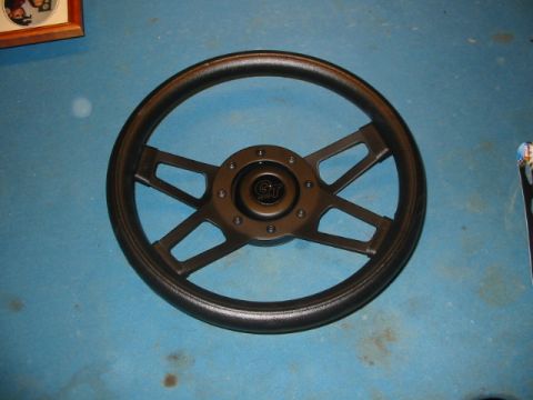 1985 Ford Crown Victoria LTD - A black steering wheel with a GT logo is shown against a blue background.