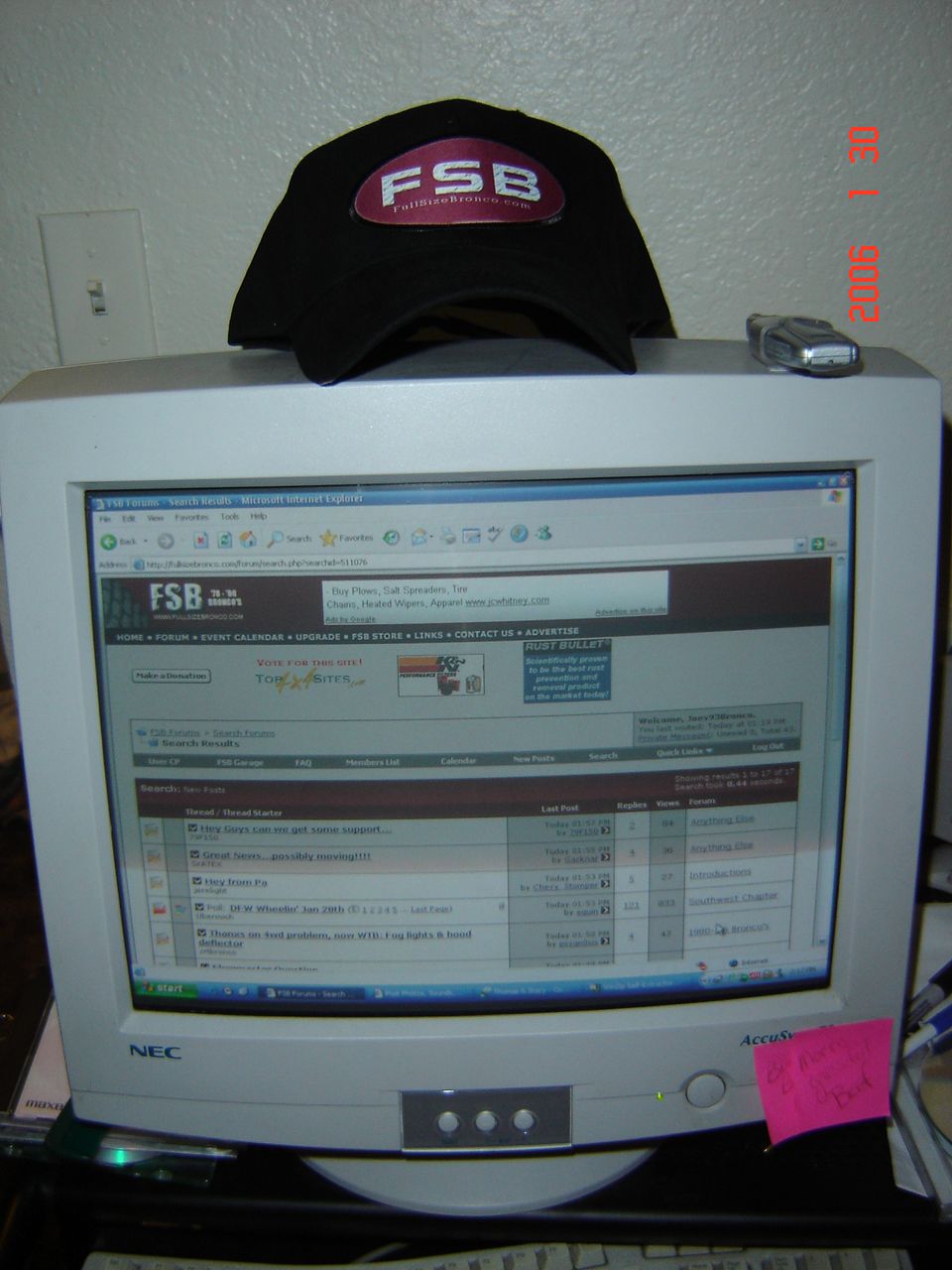 NEC monitor with a black baseball cap on top, displaying a website with forum posts