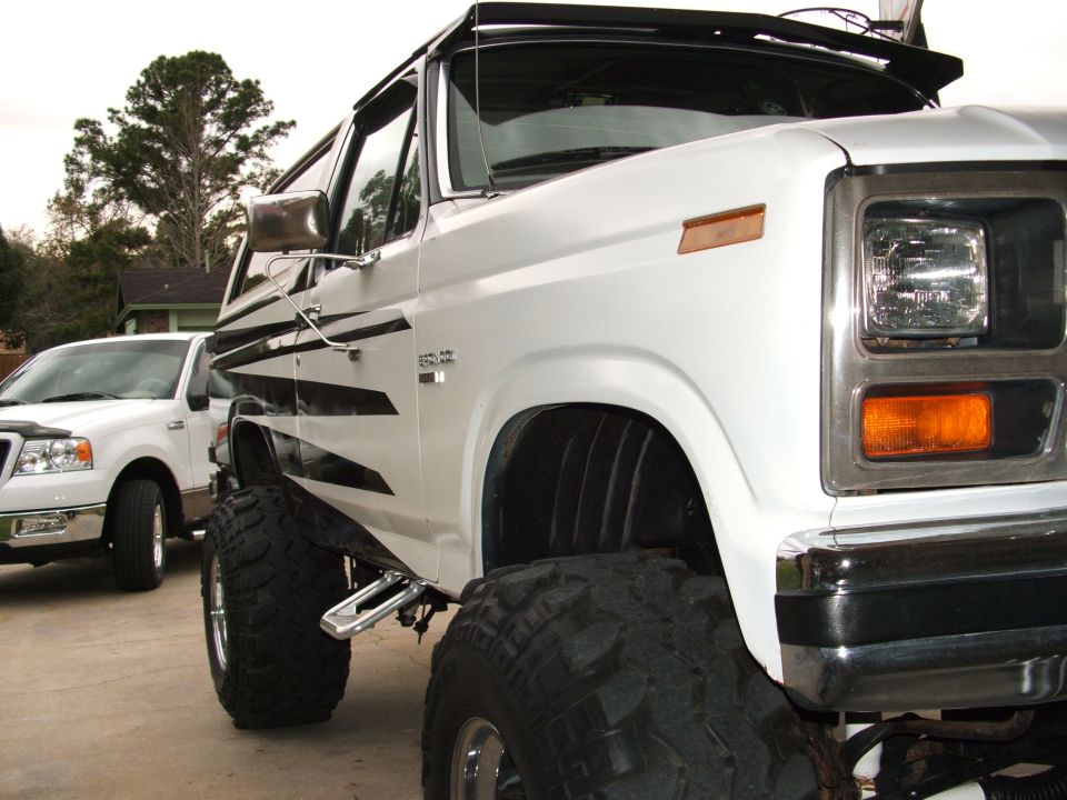 White SUV with black stripes and large tires parked next to a white pickup truck