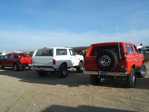 1988 Ford Bronco - Two SUVs and a pickup truck are parked on a sandy surface under a clear blue sky.