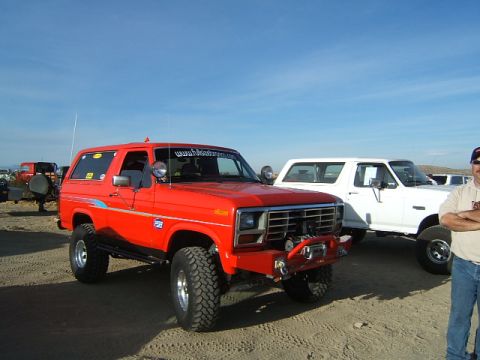 1988 Ford Bronco - Two Ford Broncos parked outdoors on a sandy surface under a clear blue sky.