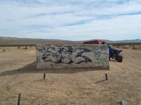 1988 Ford Bronco - Desert scene with graffiti-covered barrier, quad bike, and SUV.