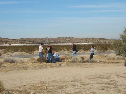 1988 Ford Bronco - A group of people are gathered by the side of a highway, seemingly engaged in a cleanup effort in a dry, desert environment.
