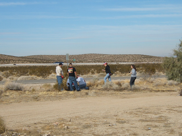 People cleaning up roadside near a highway in a desert landscape