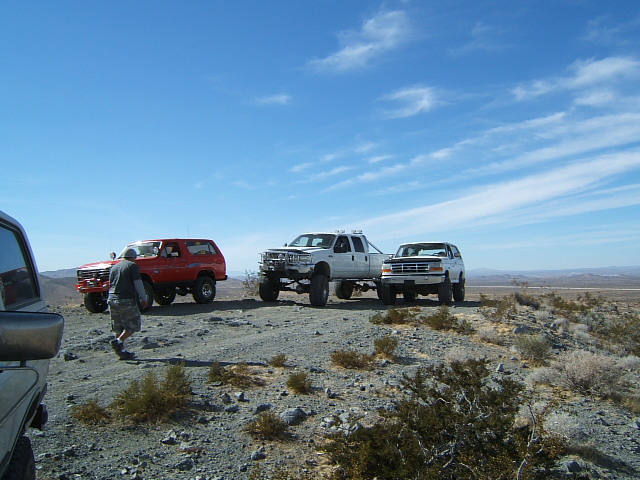 Red SUV and white pickup truck parked on a rocky hill under a blue sky