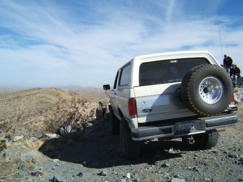 1988 Ford Bronco - A white Ford Bronco is parked on a rocky desert landscape under a blue sky with scattered clouds.