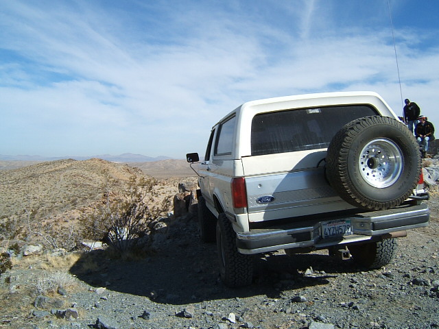 White Ford Bronco parked on a rocky incline, rear view, spare tire on back, license plate 4YZH572