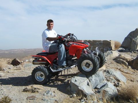 1988 Ford Bronco - A man rides a red Honda ATV through a rocky, desert landscape.