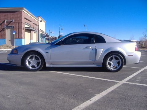 2003 Ford Mustang - A silver 2003 Ford Mustang is parked in a lot under a clear blue sky.