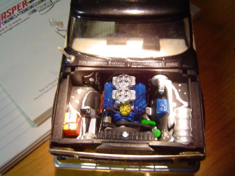 1979 Ford Bronco - Model car engine bay detail, showing a V8 engine and surrounding components. A document is partially visible.