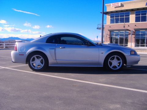 2003 Ford Mustang - A silver 2003 Ford Mustang is parked in a lot with a building in the background.