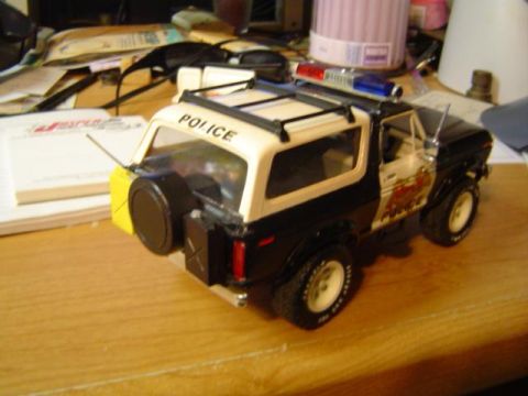 1979 Ford Bronco - A model police vehicle sits on a wooden desk amongst papers and office supplies.