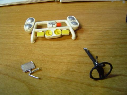 1979 Ford Bronco - Unassembled model parts, including a dashboard with lights and a steering wheel, are laid out on a wooden surface.
