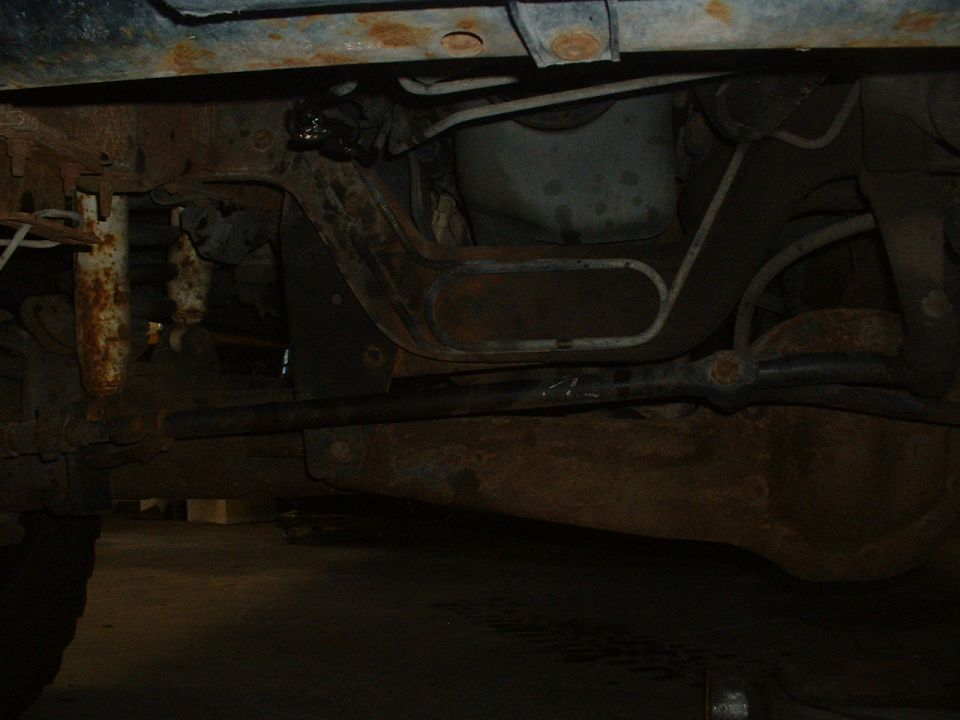 Underside of a vehicle showing rusty frame and suspension components