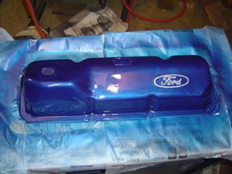 1979 Ford Bronco - A blue Ford valve cover with a white oval logo is shown during a spray painting process.