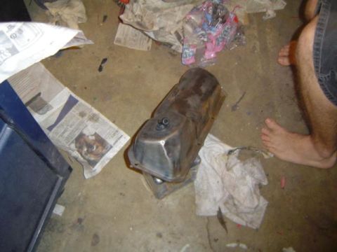 1979 Ford Bronco - A metal valve cover sits on a concrete floor amidst scattered newspapers and rags.