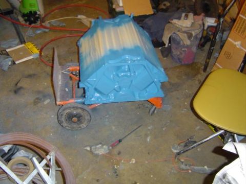 1979 Ford Bronco - Engine block painted blue and yellow sits on a cart in a cluttered garage setting.
