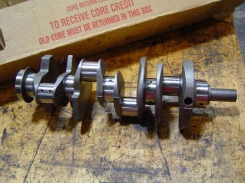 1979 Ford Bronco - A crankshaft sits on a worn wooden surface, with a cardboard box indicating a core return.