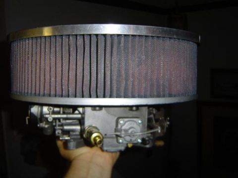1979 Ford Bronco - A hand holds a carburetor with a large, round air filter attached.