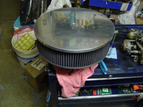 1979 Ford Bronco - A round air cleaner assembly sits on a pink towel next to a carburetor on a workbench.