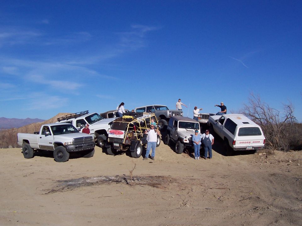 Several off-road vehicles parked on a dirt hill with people around them