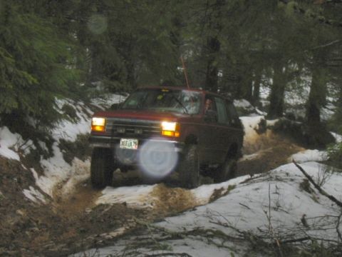 1991 Ford Explorer - A red 1991 Ford Explorer navigates a muddy and snowy trail through a forest.