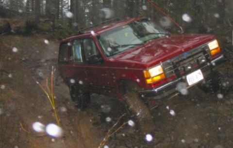 1991 Ford Explorer - The vehicle navigates a challenging, wet, off-road course with trees and mud visible.