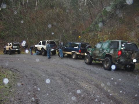 1991 Ford Explorer - A group of off-road vehicles are gathered on a dirt road in a wooded area.