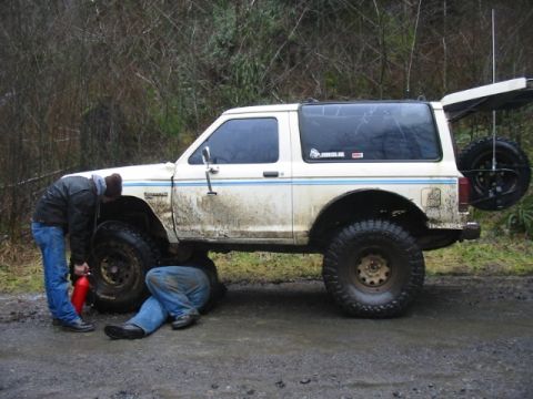 1991 Ford Explorer - Two individuals attend to a white SUV, which has a spare tire mounted on the rear and a blue stripe along its side. The registry identifies…