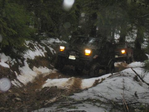 1991 Ford Explorer - Two SUVs, including a 1991 Ford Explorer, drive through a challenging snowy and muddy forest path.