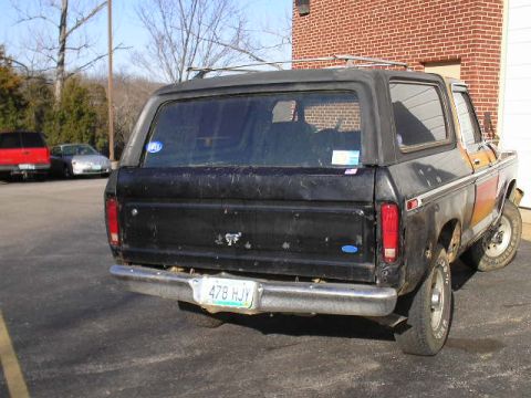 1979 Ford Bronco - This black Ford Bronco, seen from the rear, features distinctive orange and red side panels and a visible license plate.