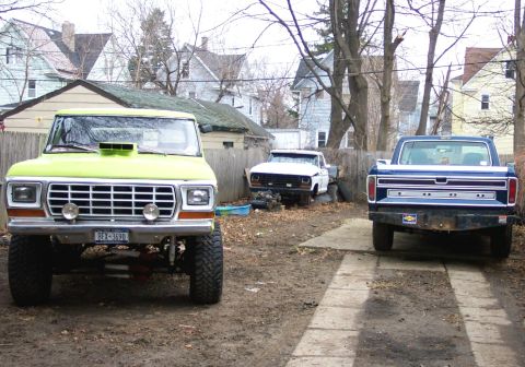 1975 Ford F-150 - Three pickup trucks are parked in a residential yard on a cloudy day.