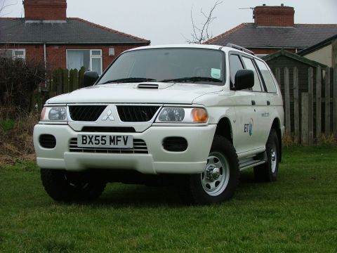 2006 Mitsubishi L200 - This white SUV, identified by its license plate BX55 MFV, features a distinctive hood scoop and is parked on a grassy lawn.