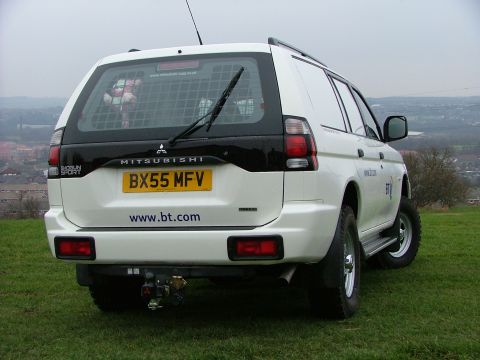 2006 Mitsubishi L200 - Rear view of a white Mitsubishi Pajero Sport SUV with a tow hitch, parked outdoors on a grassy hill.
