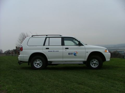 2006 Mitsubishi L200 - A white van with BT branding is parked on a grassy hill under an overcast sky.