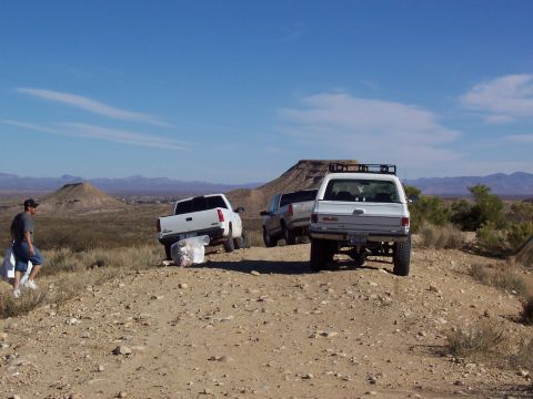 1981 Ford F-150 - Several pickup trucks are parked on a dusty trail in a dry, mountainous region under a clear blue sky.
