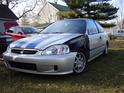 1997 Ford Taurus - Silver Honda Civic hatchback with blue stripes and a damaged fender is parked outdoors.
